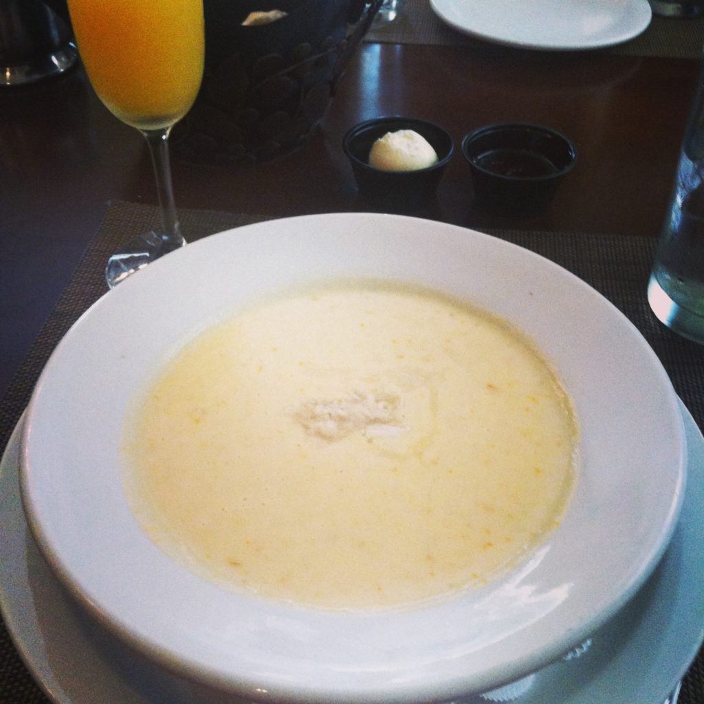 A white bowl on a plate holds a light yellow soup with lump crab on top