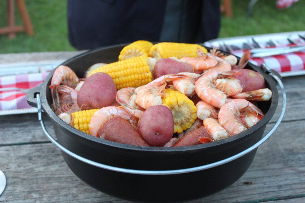 A black cast iron pot holds boiled shrimp, potatoes, and corn