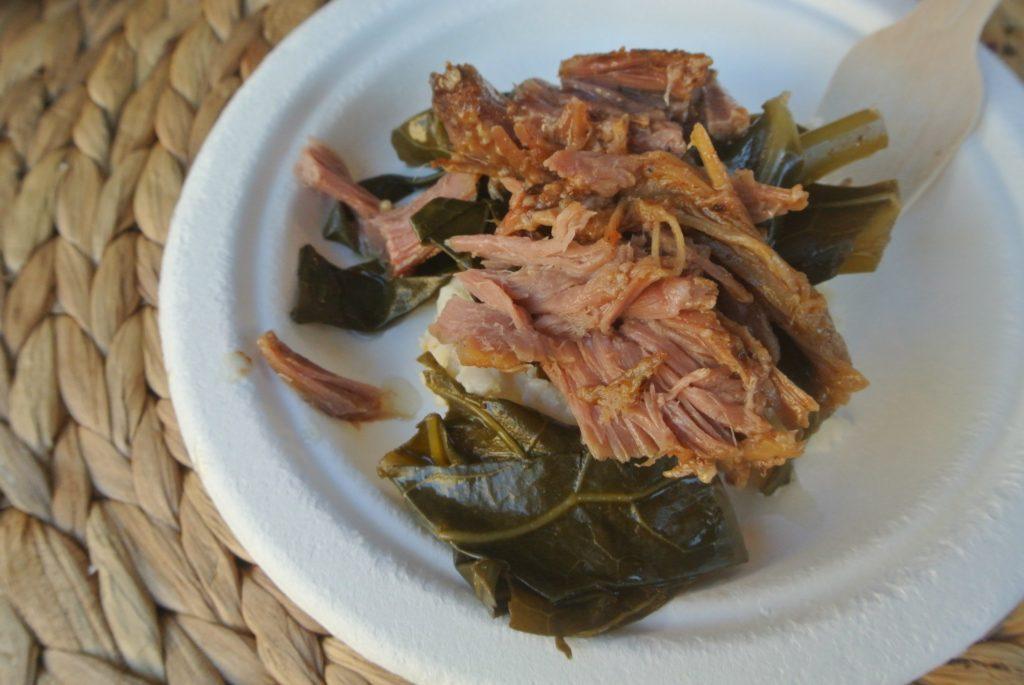 A small paper plate has pieces of collard greens with pulled pork atop